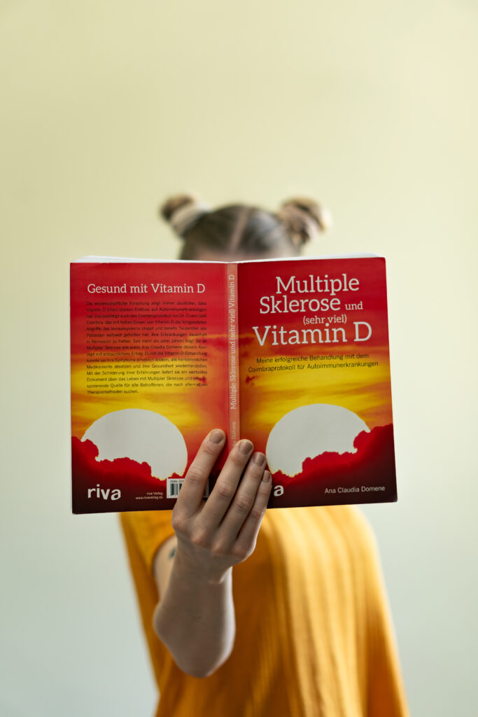 Junge Frau, die ein Buch mit der Aufschrift "Multipler Sklerose und Vitamin D" in die Kamera hält.
