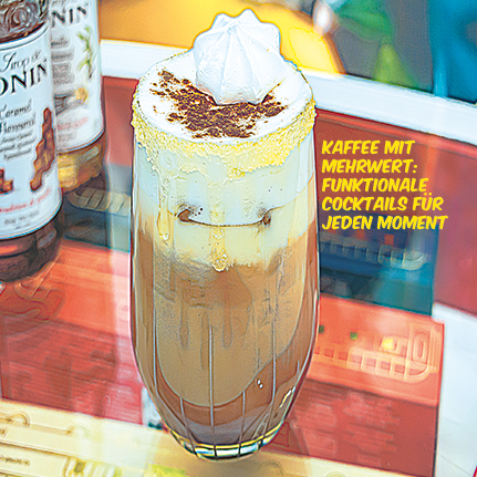 Eisgekühlter Schichtkaffee mit Sahnehaube, Kakaopulver und gelbem Zuckerrand, auf einem bunt reflektierenden Tisch, daneben Sirupflaschen.